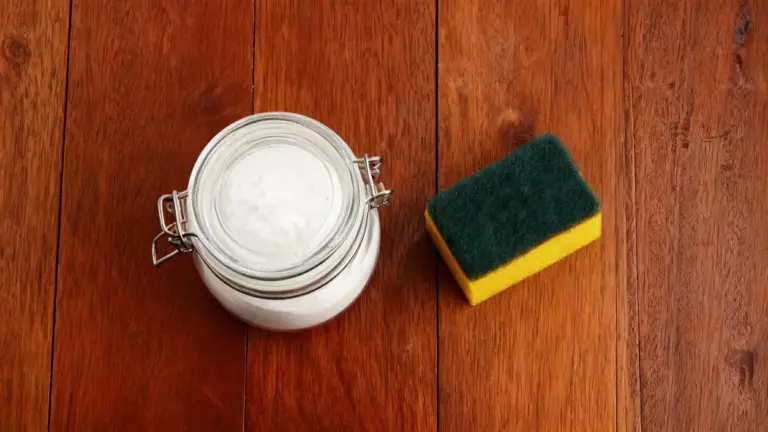 Barattolo con polvere bianca e una spugna da cucina su una superficie in legno