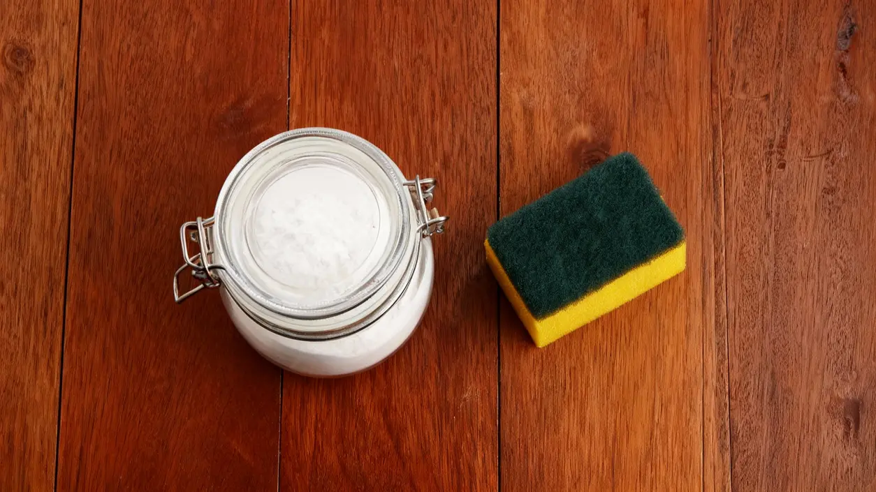 Barattolo con polvere bianca e una spugna da cucina su una superficie in legno