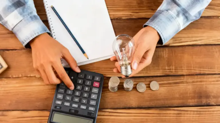 Persona con calcolatrice, lampadina e monete su un tavolo di legno