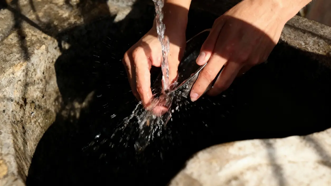 Mani che lavano un piatto sotto acqua corrente in un lavandino di pietra