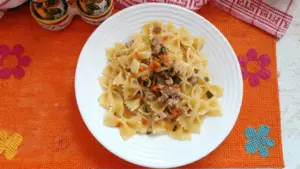 Piatto di farfalle con ragù bianco di salsiccia e funghi servito su tovaglietta arancione