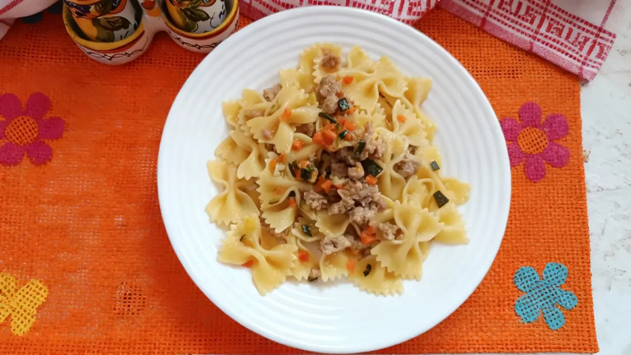 Piatto di farfalle con ragù bianco di salsiccia e funghi servito su tovaglietta arancione