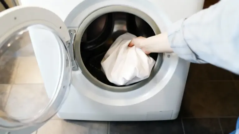 Una persona inserisce un lenzuolo bianco in una lavatrice a carica frontale